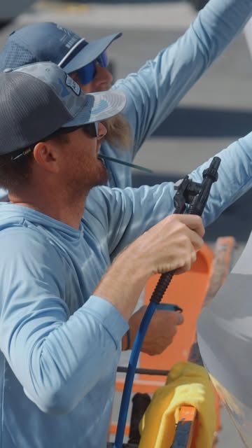 Crew member polishing a dark yacht hull with a rotary polisher